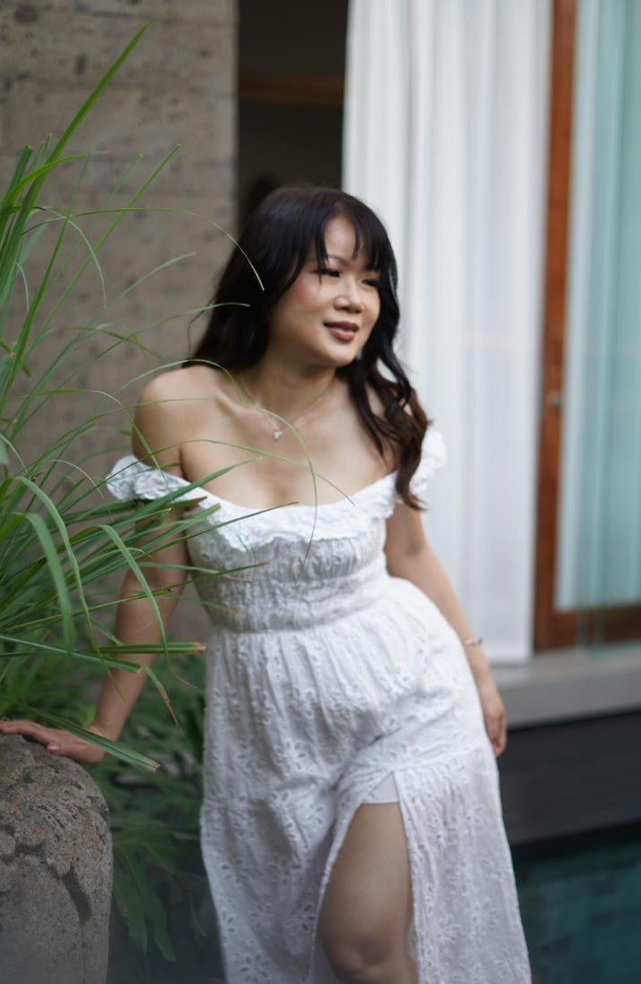 Woman in a white dress standing outdoors with plants and a building in the background