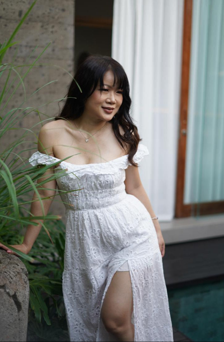 Woman in a white dress standing outdoors near a building and plants.
